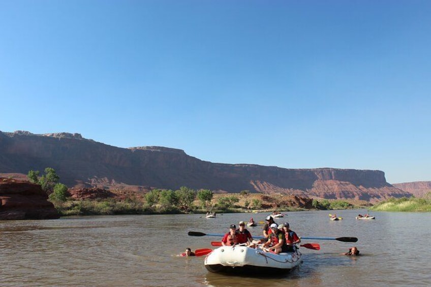 A group of people rafting on a river with red rock formations in the background. 1