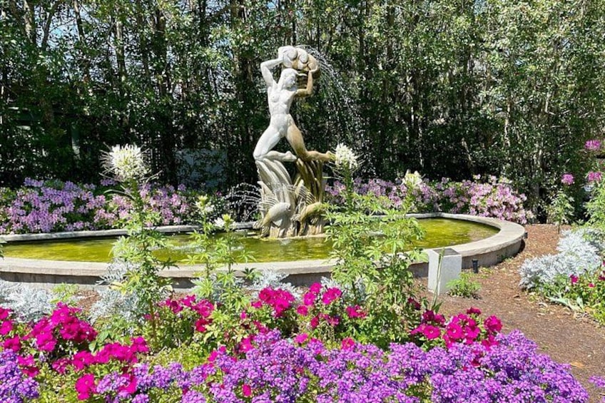 A garden with a statue of a woman holding a child, surrounded by vibrant flowers and a pond. 2