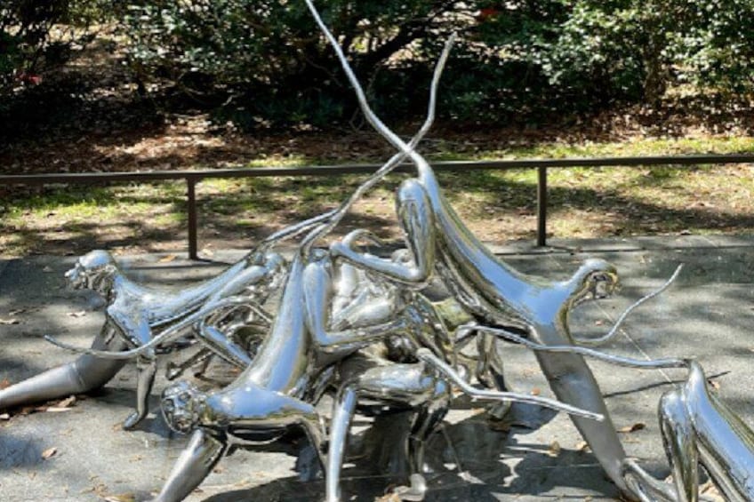A metallic sculpture of intertwined figures in an outdoor setting. 4