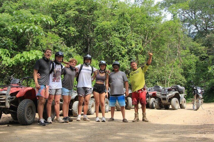 A group of people standing in a forested area with off-road vehicles in the background. 1