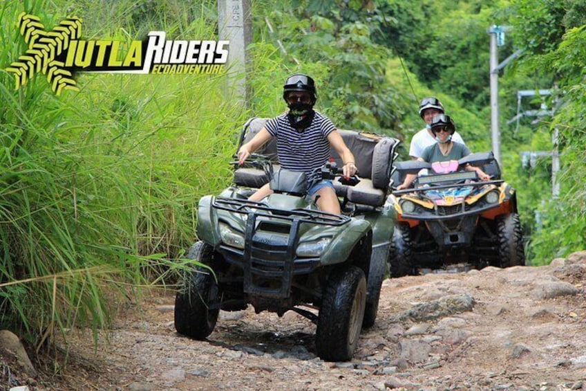 Two people riding ATVs on a dirt path surrounded by greenery. 4