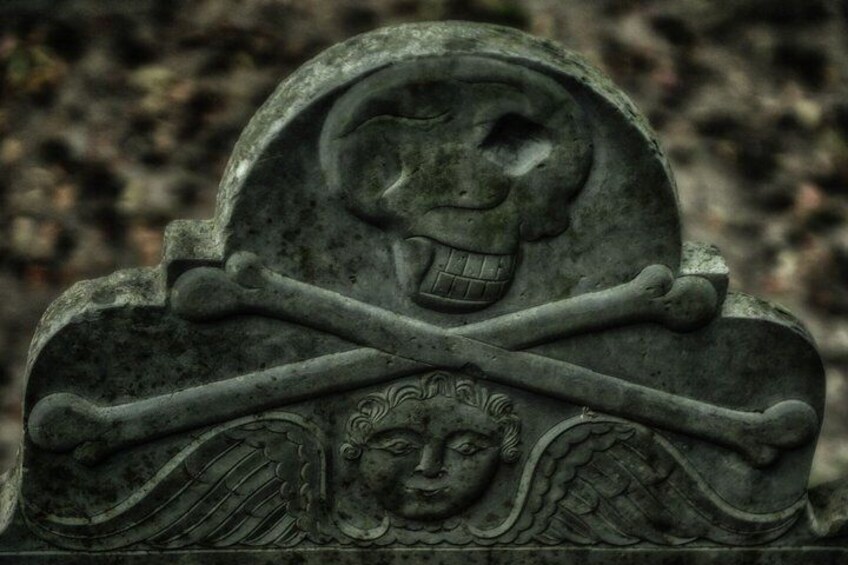 A tombstone with a skull and crossed swords, an angelic figure, and a face. 3