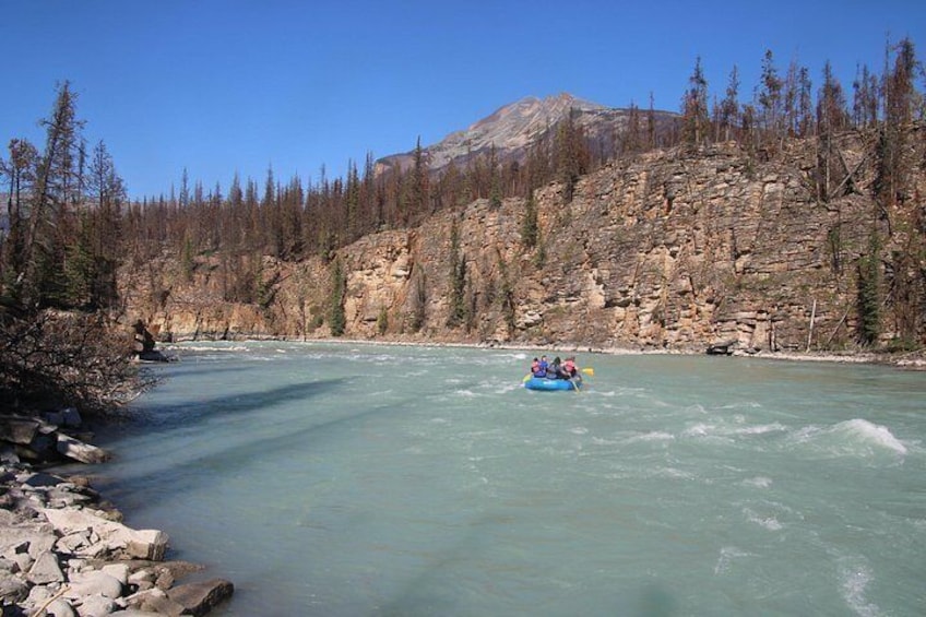 A river with a raft, rocky cliffs, and sparse trees. 5
