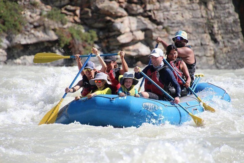 A group of people in a blue raft navigating through white water rapids. 2