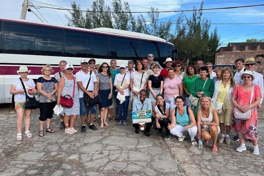 A group of people posing in front of a bus on a paved surface with trees in the background. 3