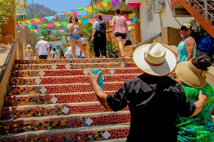 Un escalier orné de carreaux colorés, une personne portant un t-shirt et un chapeau noirs, et une femme en robe verte. 3