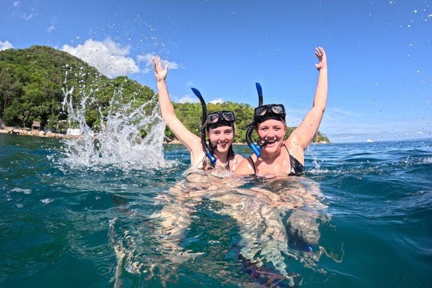 Twee personen snorkelen in helderblauw water, met een bergachtig landschap op de achtergrond. 2