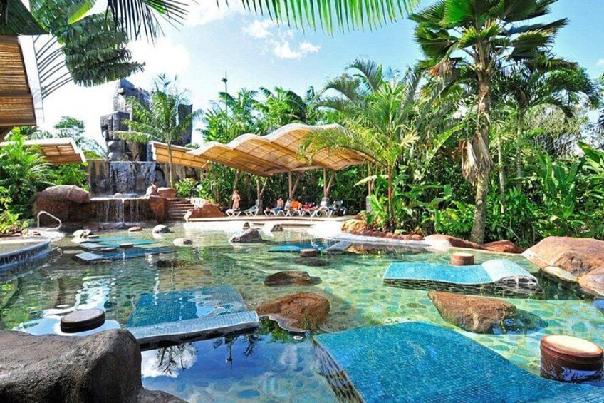 Una piscina tropicale con acqua cristallina, rocce, palme e una cascata. 4