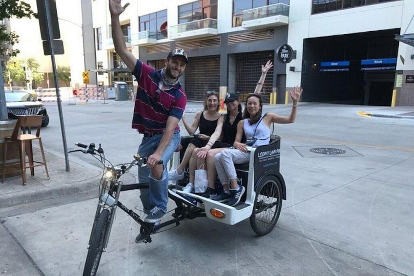 Une personne à vélo, tirant une charrette avec trois passagers, avec un bâtiment en arrière-plan. 2