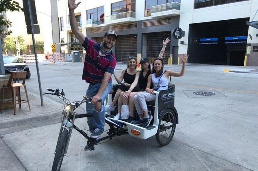 Un homme à vélo, tirant une charrette dans laquelle sont assis trois autres individus, avec un bâtiment visible en arrière-plan. 3