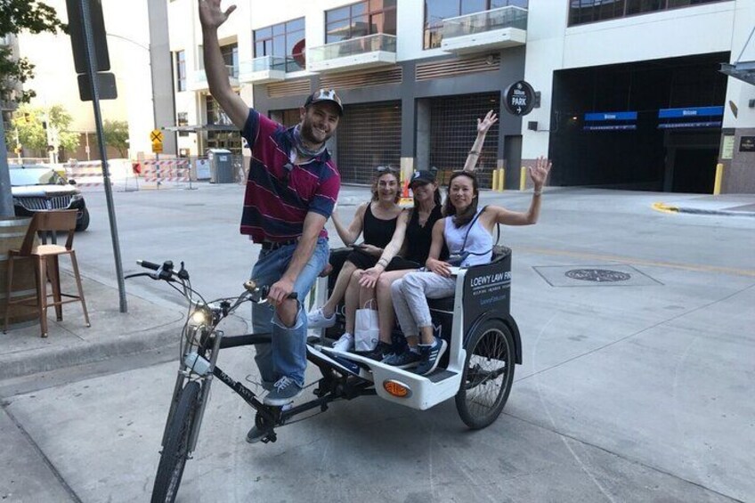 Una persona in bicicletta con un carretto, tre passeggeri e un edificio sullo sfondo. 5