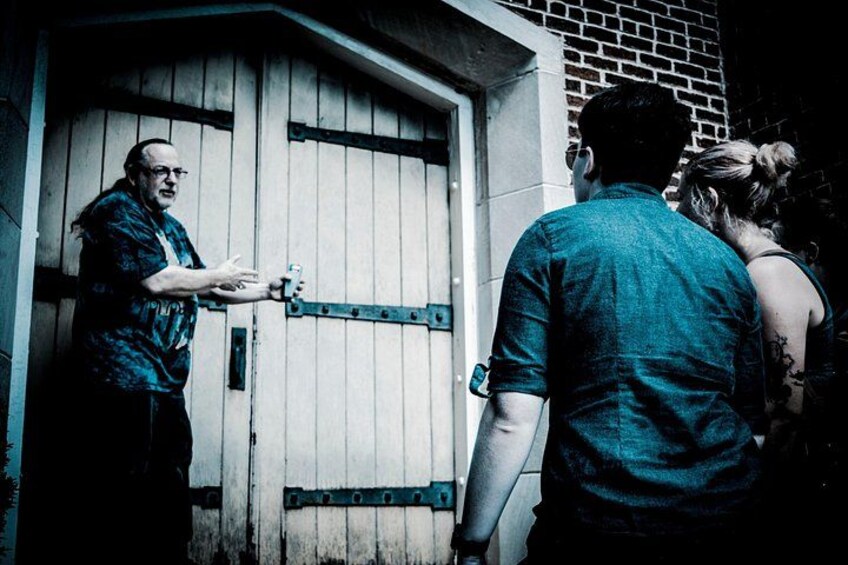 A man handing a key to a woman, standing in front of a wooden door with metal hinges. 1