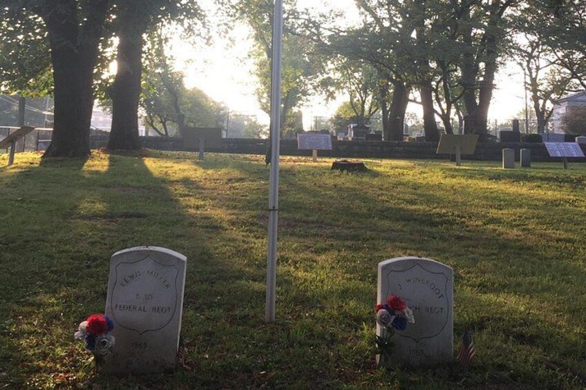 Dos lápidas en un cementerio, con árboles al fondo. 3