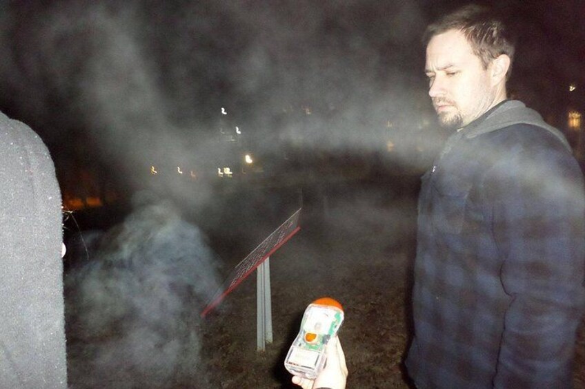 Una persona sostiene una botella con etiqueta, de pie junto a un objeto rojo sobre una superficie oscura. 5