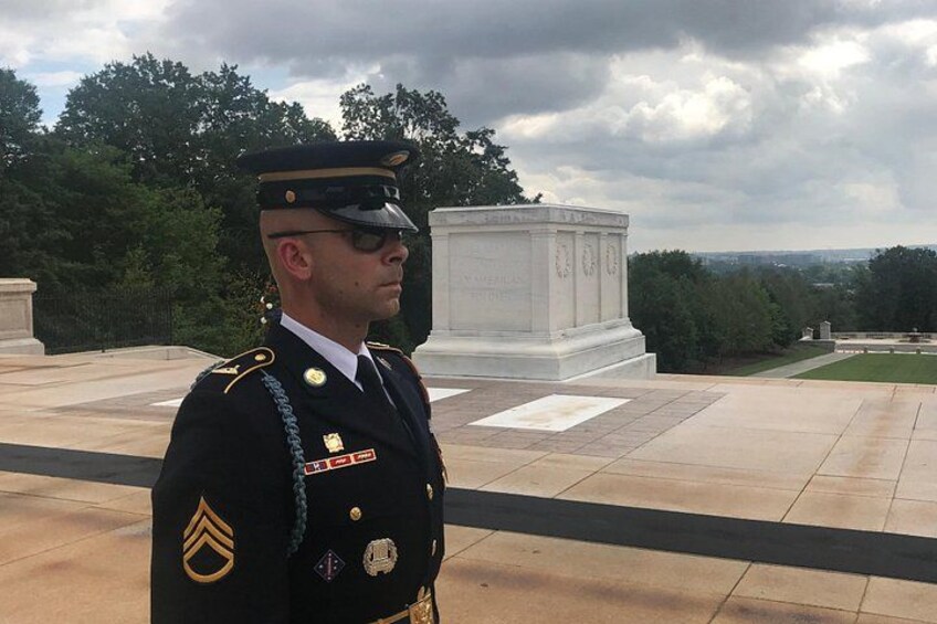A uniformed individual standing in front of a memorial with a cloudy sky in the background. 3