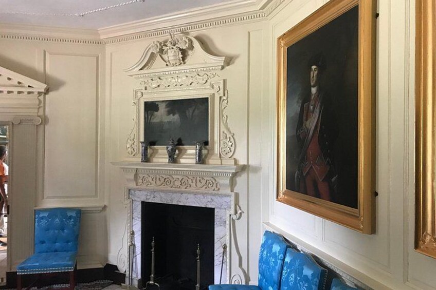 A room with a white fireplace, a blue armchair, and a large framed portrait on the wall. 2