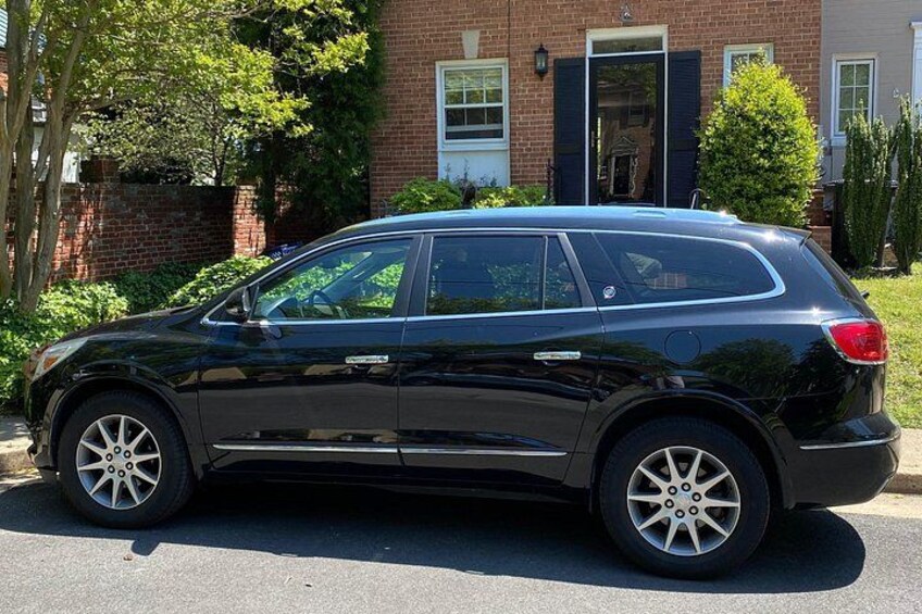 A black SUV parked on a street in front of a brick house with a black door and windows. 4