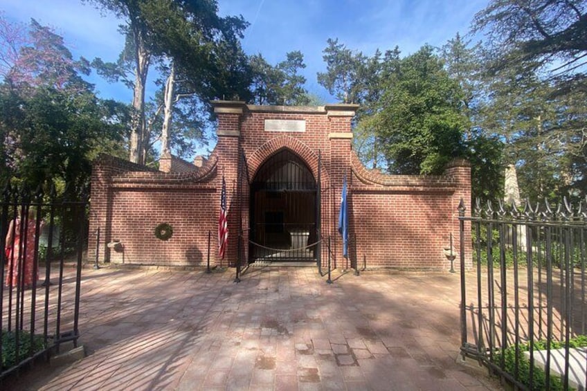 A brick entrance gate with an American flag, surrounded by trees and a clear sky. 2