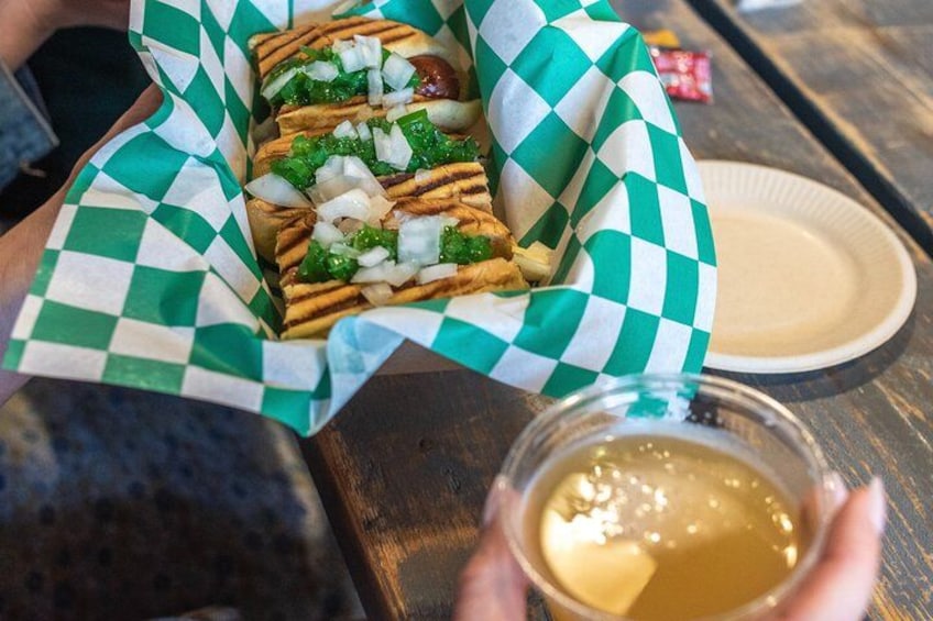 A grilled sandwich with toppings, held in a paper tray, and a small cup of sauce. 2