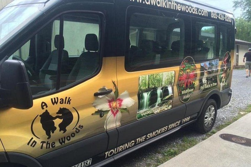 A yellow van with 'A Walk in the Woods' and 'Guided Nature Walks' text, parked on a street. 1