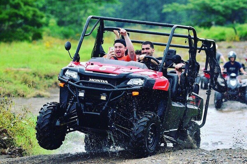 A red Honda ATV driving through a muddy path with passengers. 3
