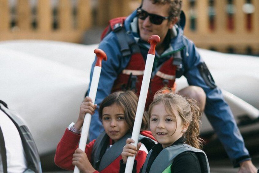 Two children holding poles, a person in a blue jacket, and a white vehicle in the background. 2