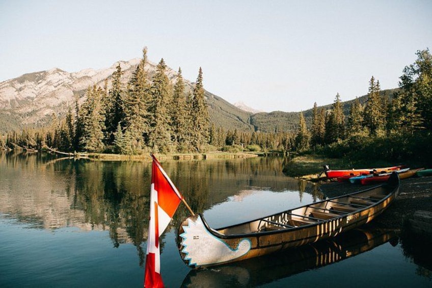 A calm lake with a canoe and a flag, surrounded by dense forest and mountains. 5