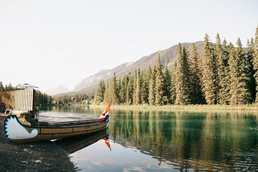 A wooden boat with a flag on a calm lake surrounded by trees and mountains. 4