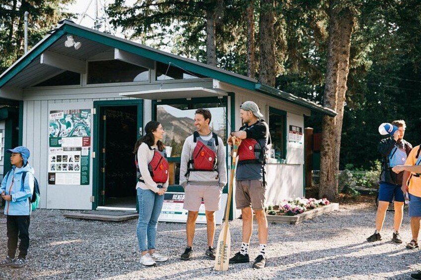 A group of people standing in front of a small building with a green roof, surrounded by trees. 3
