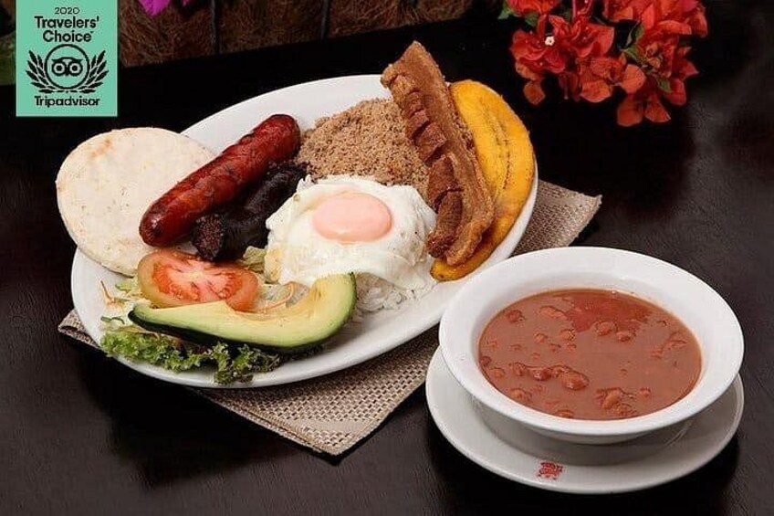 A plate of food including a fried egg, sausage, avocado, and a bowl of soup. 1