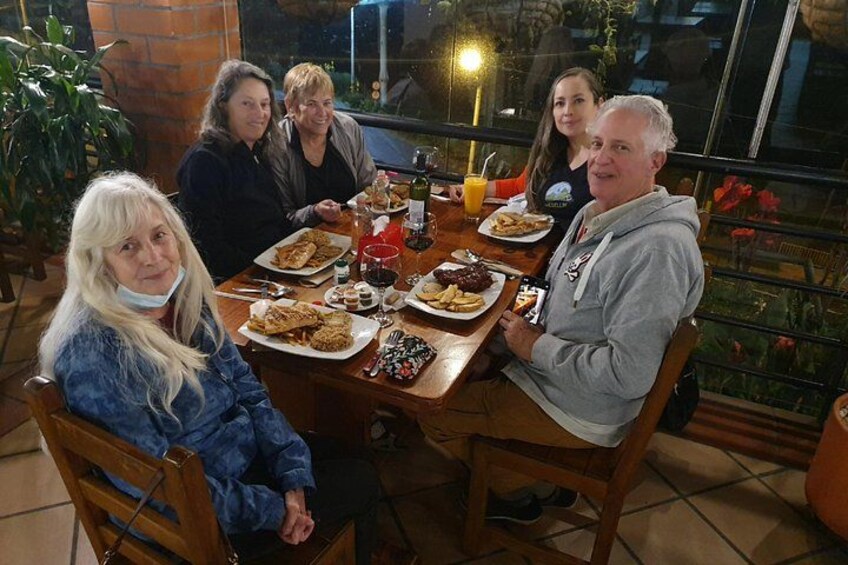 A group of people dining at an outdoor table with various dishes and drinks. 3