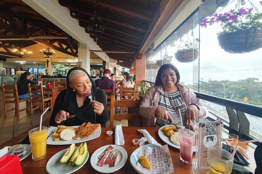 Two people dining at a restaurant with a view, plates of food, and drinks on the table. 5