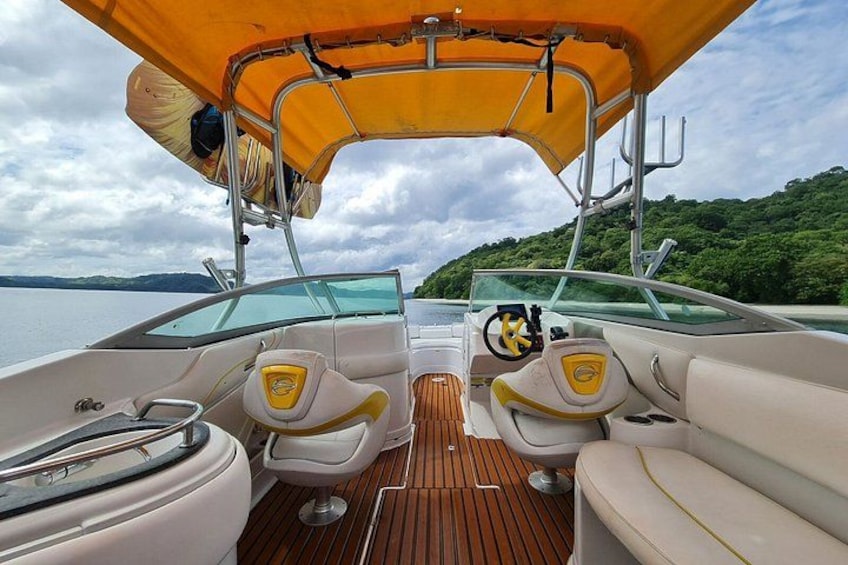 A boat's interior with a wooden deck, two white cushioned seats, a steering wheel, and a canopy. 2