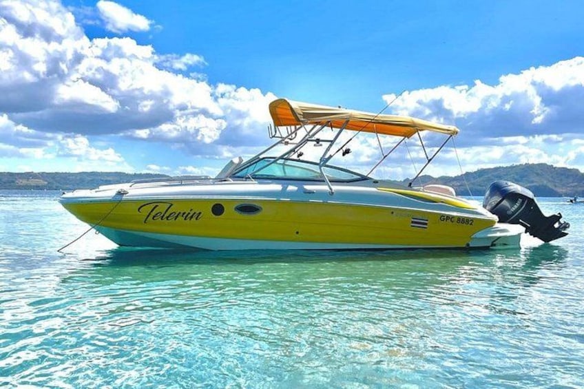 A yellow boat named 'Telerin' with a canopy, on clear blue water with a mountainous landscape in the background. 5