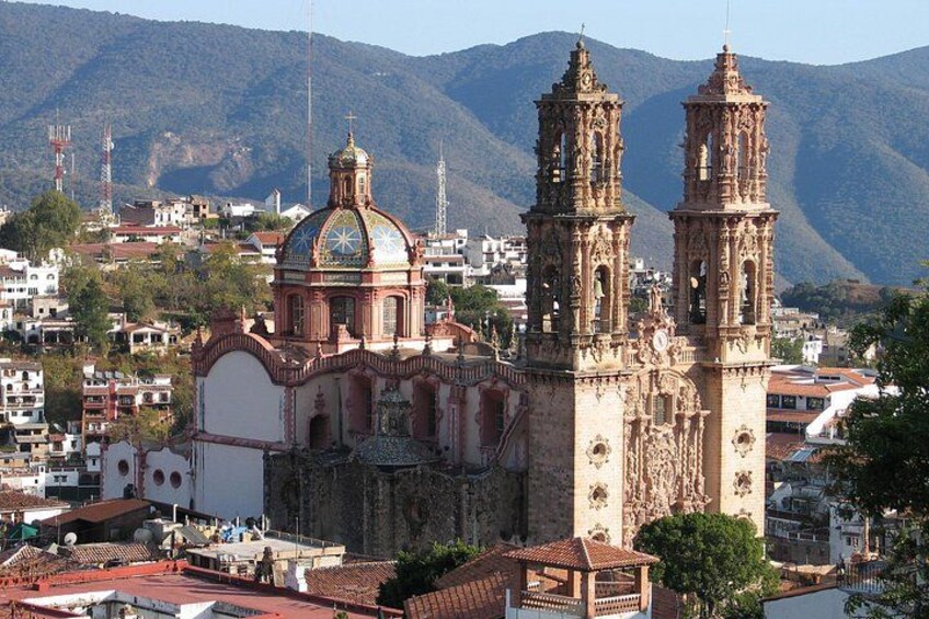 A historic church with two bell towers, surrounded by a mountainous landscape and urban buildings. 1