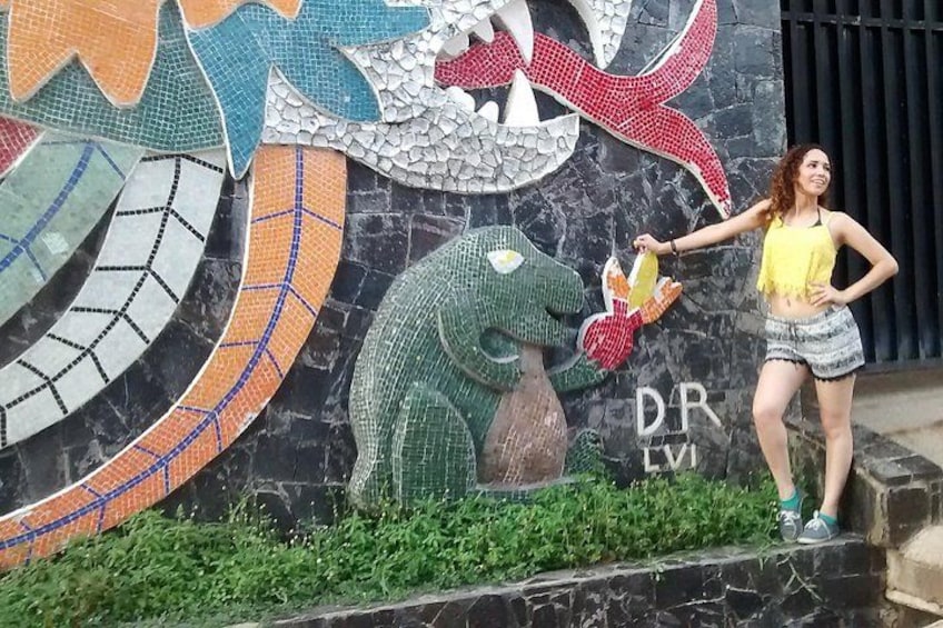 A mosaic mural with a dinosaur and a person standing in front of it. 2
