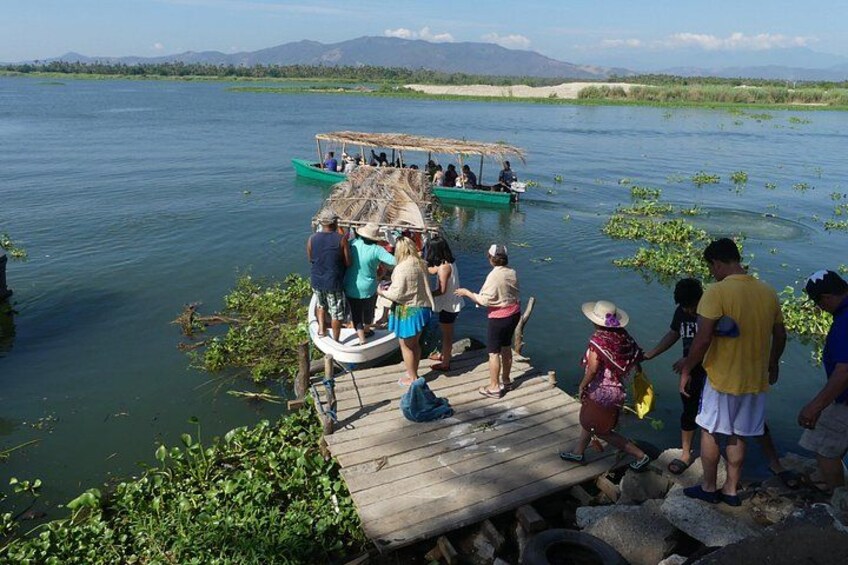 A group of people on a dock, a boat on the water, and a river with greenery. 2