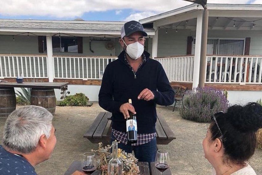A person pouring wine into a glass at an outdoor table with a house in the background. 3