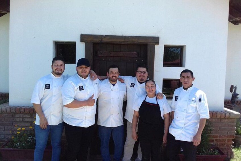 A group of chefs standing in front of a building with a wooden door and windows. 4