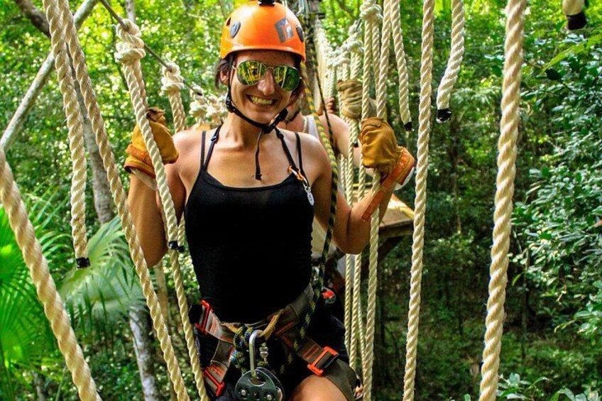 Une personne qui fait de la tyrolienne à travers une forêt, avec des cordes et une végétation luxuriante. 1