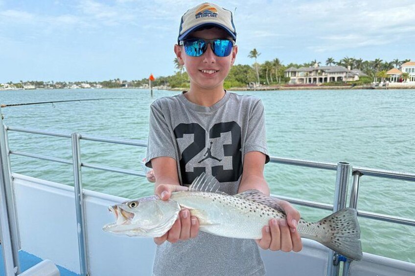 A person holding a fish on a boat with a water body and houses in the background. 5