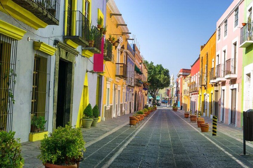 Una calle colorida flanqueada por edificios, plantas en macetas y un cielo despejado. 3