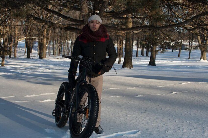 Una persona de pie junto a una bicicleta en un parque nevado con árboles desnudos. 2