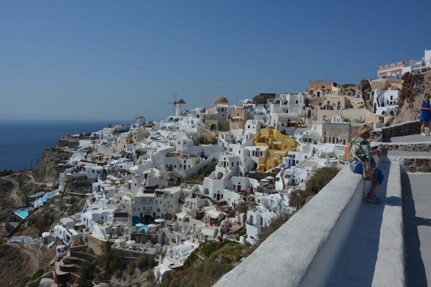 A coastal village with white buildings, a windmill, and a person sitting on a ledge. 3