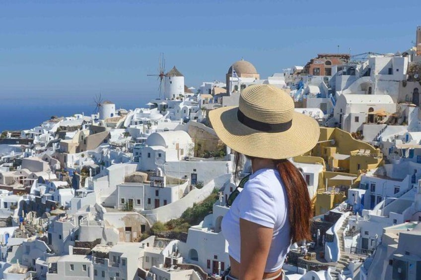 A woman in a straw hat overlooking a white-washed town with windmills and domed buildings. 1