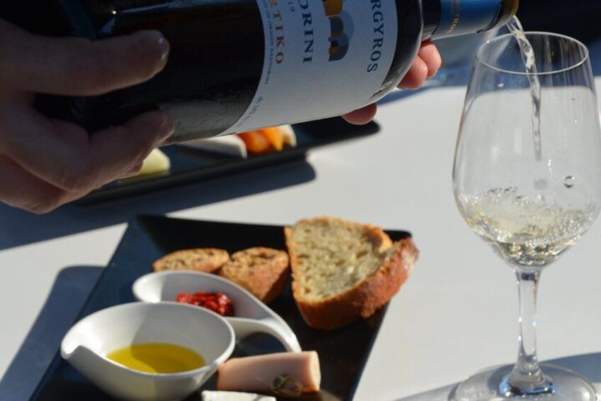 A person pouring wine into a glass. There are slices of bread and a small bowl of sauce on a plate. 5