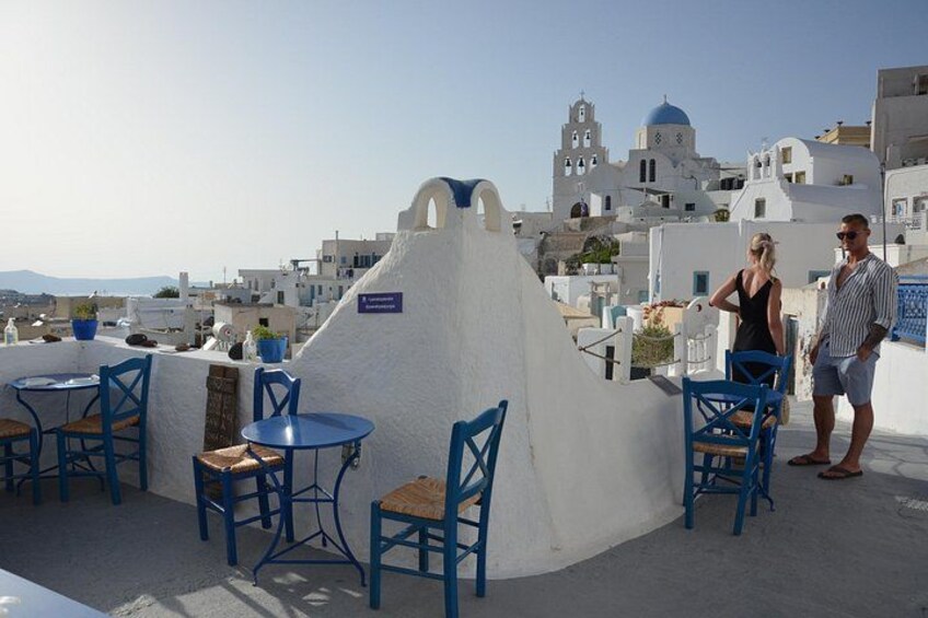 Une terrasse sur le toit, avec des chaises et des tables bleues, un mur blanc et une vue sur des bâtiments blancs surmontés de coupoles bleues à l’arrière-plan. 4