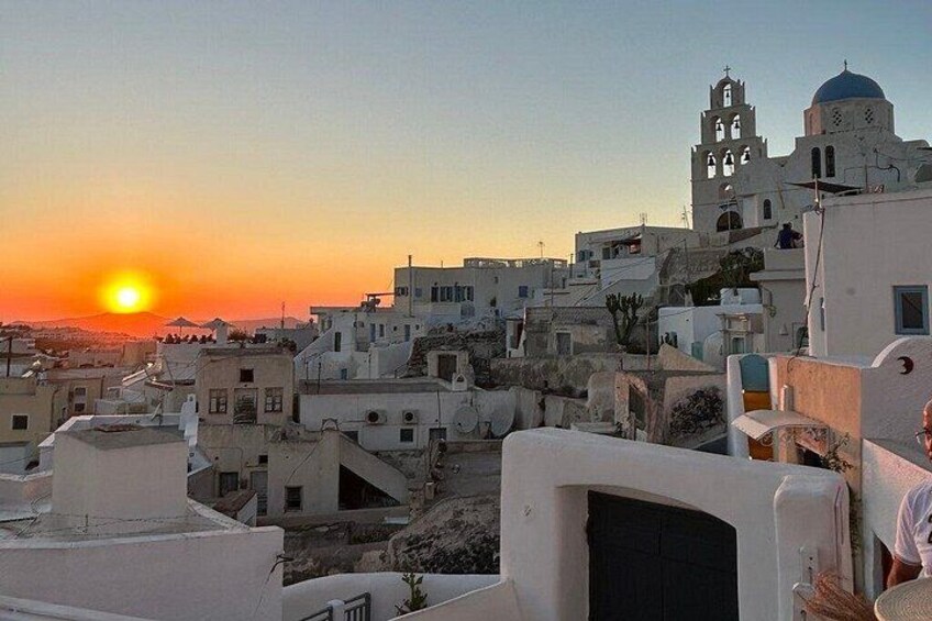 Une ville côtière au coucher du soleil, avec des bâtiments blancs, une église imposante surmontée d’un dôme bleu et un ciel dégagé. 3