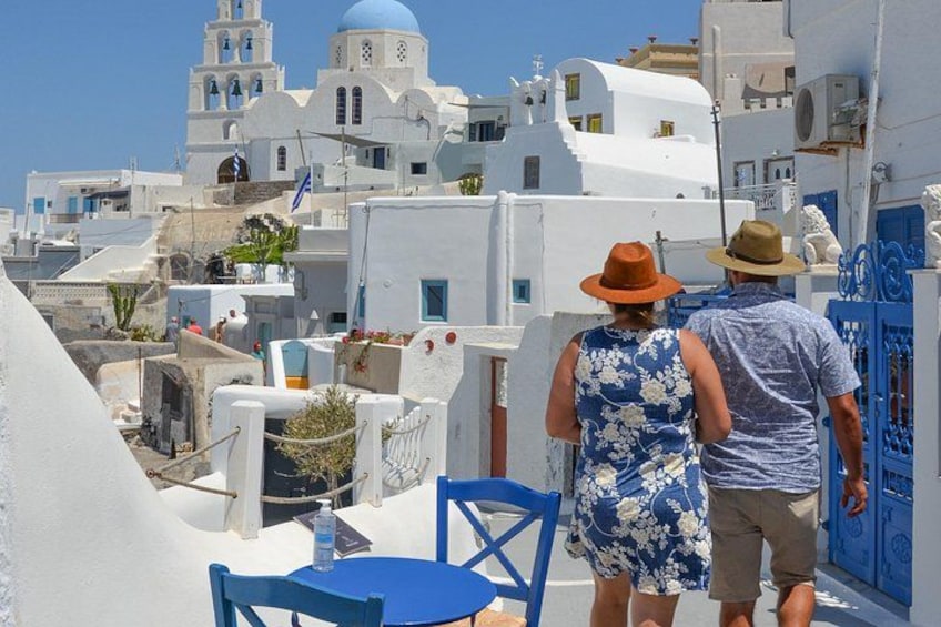 A couple standing on a rooftop overlooking a white-washed town with blue doors and domed buildings. 4