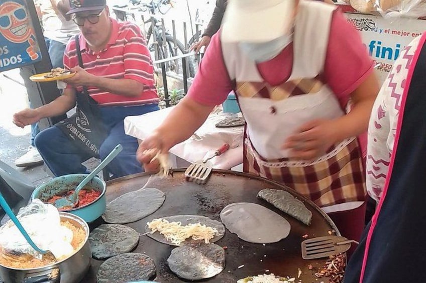 A street food vendor cooking on a griddle with tortillas, a bowl of sauce, and a plate of food. 5